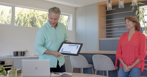 Senior Couple Joyously Celebrating Over Framed Certificate in Modern Kitchen