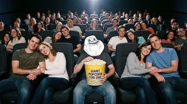 Sitting alone with forever alone mask holding giant popcorn in crowded movie theater