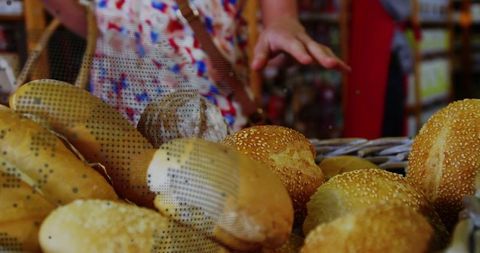 Customer reaching for sesame rolls in wicker basket at artisanal bakery counter