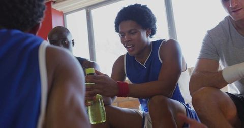 Basketball teammates sharing water bottle on bench during game huddle