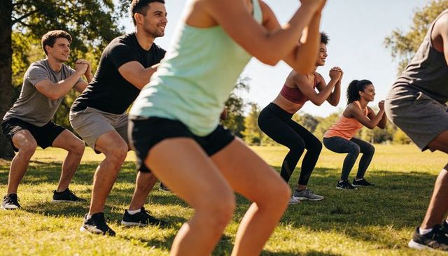 Outdoor group fitness doing squats in sunny park | diverse adults training together
