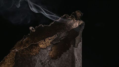 Smoldering charred metal cylinder emitting thin smoke plume with jagged rusted rim