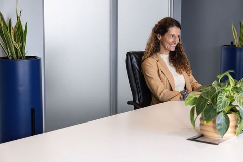 Mature businesswoman smiling while sitting at modern conference table with office plants