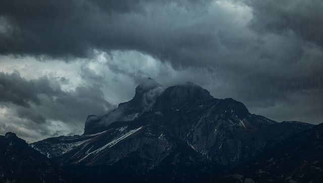 Brooding alpine massif under storm clouds with jagged peaks, mist-filled gullies and driving rain