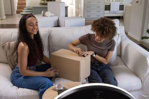 Two african american women unpacking box on sofa, moving in, smiling and sharing moment