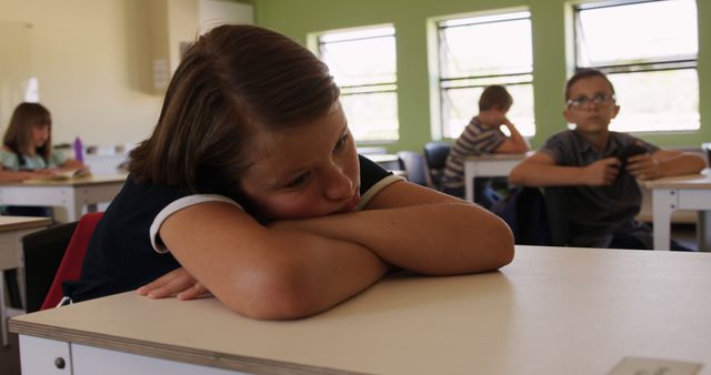 Bored caucasian girl sitting at desk resting head on arms in elementary school class. Childhood, education, learning and elementary school, unaltered.