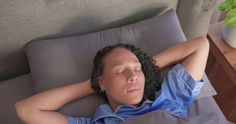 African american woman resting peacefully in bed wearing blue pajamas with curly hair