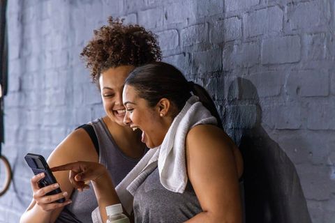 Diverse friends laughing and sharing smartphone after intense workout at urban gym