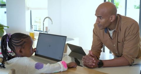 Parent teaching african american child using laptop at kitchen island for home learning