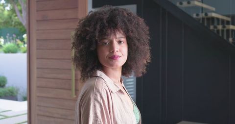 Confident african-american woman wearing tan overshirt posing in modern foyer
