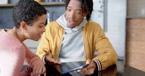 Diverse couple sharing tablet at kitchen table, casual home technology conversation