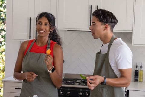 Multicultural couple cooking together in modern kitchen holding colorful pepper slices