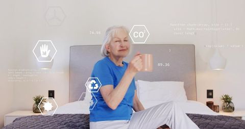 Elderly woman sipping coffee on bed wearing blue top holding mug with ar wellness icons
