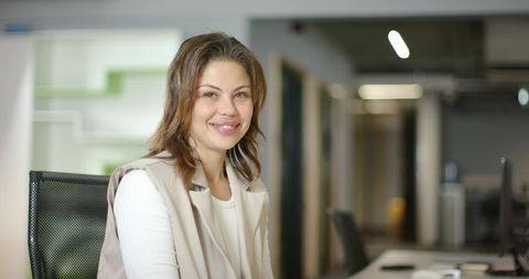 Smiling businesswoman working at modern office desk in casual white top and beige vest