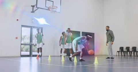 Basketball players dribbling through cone drill coach guiding skill training on court