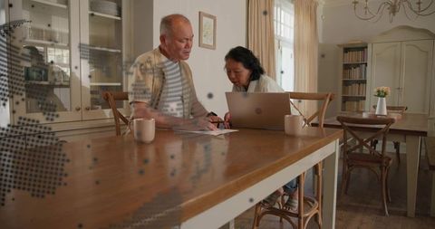 Adult son and mother reviewing documents at sunlit wooden dining table with laptop