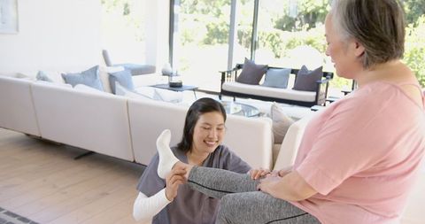 Physiotherapist Assisting Senior Woman with Leg Exercises in Living Room