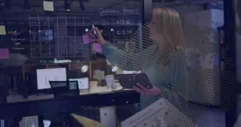 Businesswoman Writing on Glass Board While Holding Tablet in Collaborative Office
