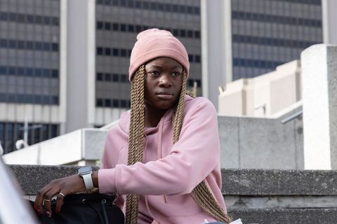 African american woman sitting on urban steps wearing pink beanie and hoodie contemplative