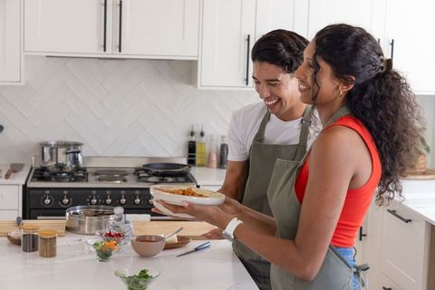 African american couple cooking and smiling while holding casserole in modern kitchen