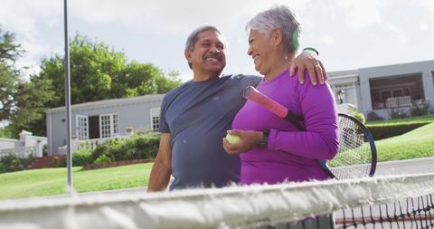 Active Senior Couple Hugging on Sunny Tennis Court