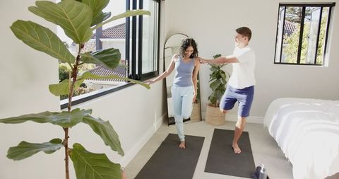 Couple Practicing Yoga Balancing Poses in Sunlit Bedroom