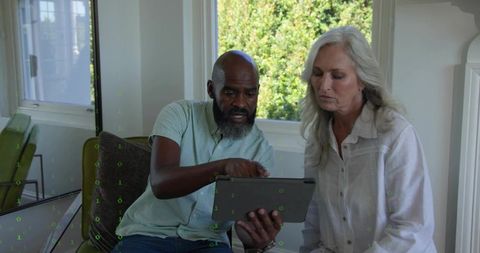 Mature couple learning tablet together, pointing at screen in bright living room