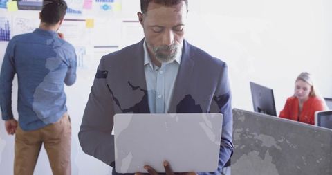 Manager holding laptop with semi-transparent world map overlay showing global business collaboration