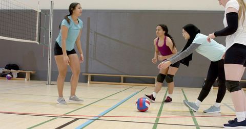 Female volleyball teammates practicing receiving drills in indoor gym showcasing teamwork