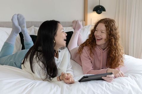 Young women laughing on bed sharing tablet cozy bedroom hangout for lifestyle friendship
