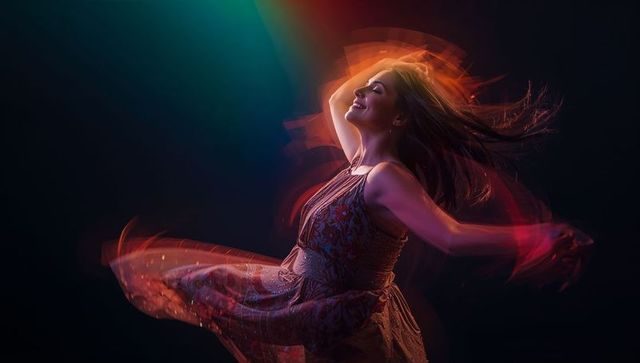 Woman twirling in patterned dress with neon light trails, dynamic motion and vibrant glow