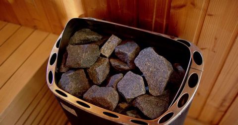 Glowing sauna stones resting in stainless steel heater basket surrounded by warm wood panels