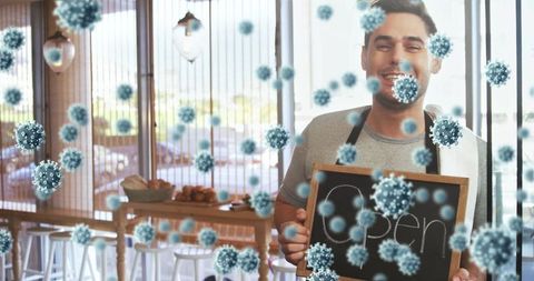 Smiling Barista Holding Open Sign in Cozy Cafe with Floating Virus Particles