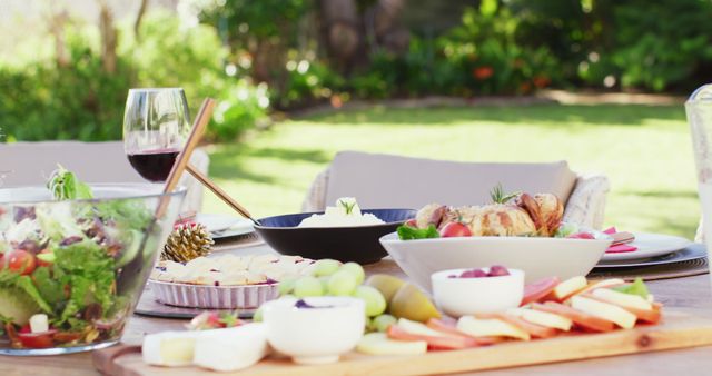 Scene showcasing an outdoor table set with a variety of foods including fresh salad, fruits, cheese platter, and glasses of wine. Perfect image for illustrating gourmet picnics, garden parties, social gatherings, or articles focused on healthy eating and leisure.