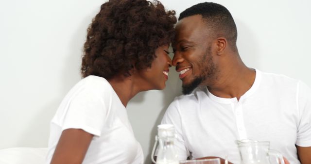 Happy couple sitting close with foreheads touching while smiling. Ideal for use in promoting relationship counseling, Valentine's Day content, family planning services, or personal relationship articles.