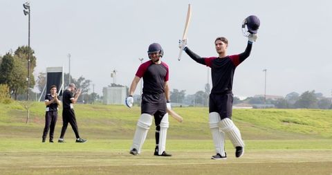 Male cricket teammates celebrating milestone with bats raised