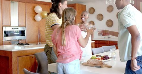 Group of friends enjoying each other's company while having drinks and snacks in a contemporary kitchen. This lively and welcoming scene is perfect for promoting friendly gatherings, lifestyle blogs, and social events. Ideal for websites or publications focusing on home entertainment and informal get-togethers.