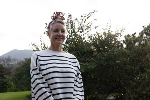 Smiling middle-aged woman wearing merry christmas headband in backlit garden
