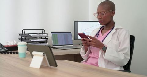 African woman doctor using smartphone while monitoring telemedicine dashboards and analytics