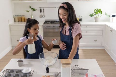 African american mother and daughter baking together pouring milk into bowl teaching kitchen skills