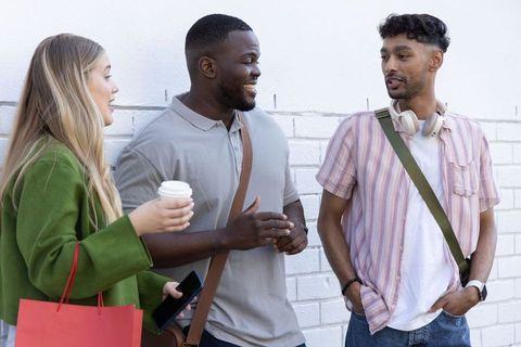 Multiracial friends chatting on urban sidewalk holding coffee cup and shopping bag smiling