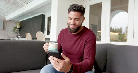 Man relaxing on sofa while checking smartphone in modern home