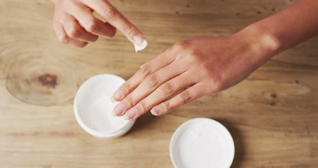Image of hands of caucasian woman moisturizing hands with cream on wooden surface. beauty and self care concept.