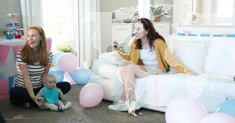 Young women celebrating baby shower with infant, pastel balloons, cupcakes, gifts