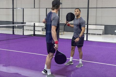 Indoor padel coaching session on vibrant purple court showing player interaction
