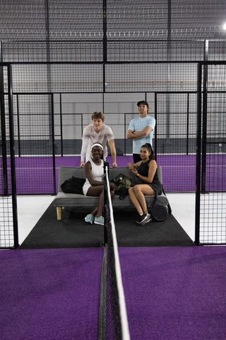 Mixed padel team posing at center court with purple turf, rackets and sports bags