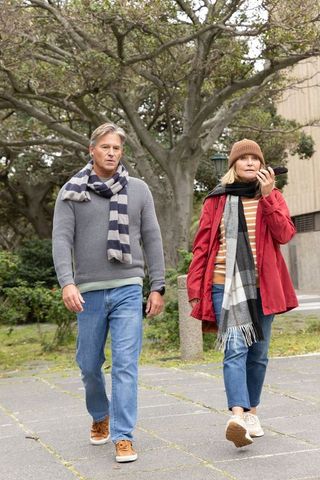 Mature couple walking urban park walkway in fall, woman talking on smartphone