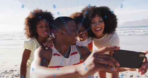 Black family taking beach selfie with smartphone, parents laughing, kids playful