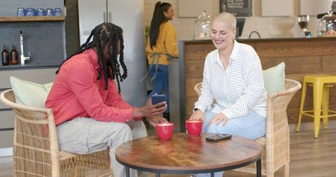 Diverse friends sharing smartphone and lattes at cozy cafe table, smiling and chatting