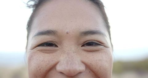 Smiling middle-aged woman closeup showing freckles, crow's feet, mole and natural skin texture
